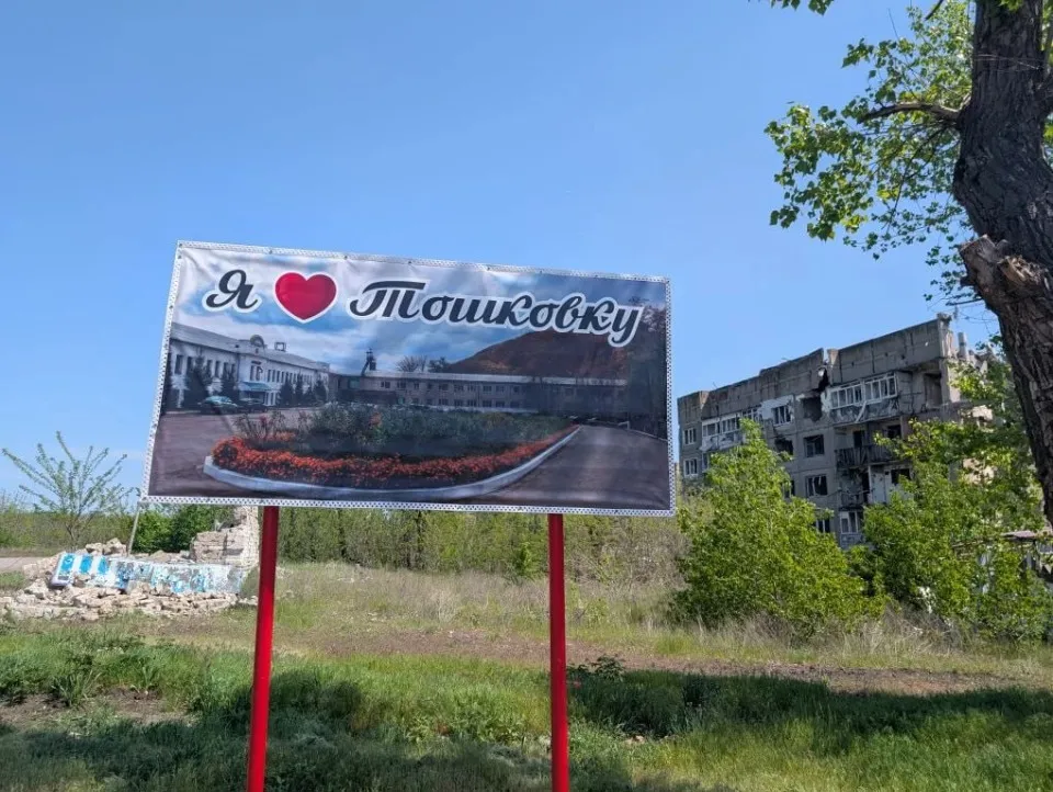 Білборд Я люблю Тошківку на тлі зруйнованого населеного пункту