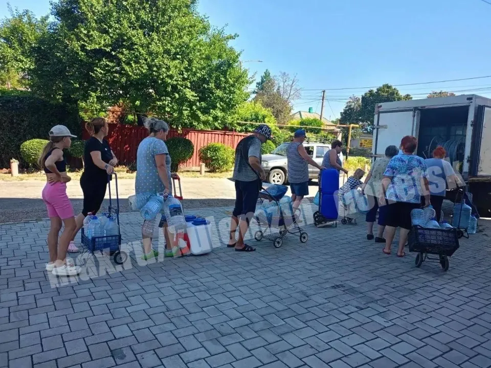 Люди стоять у черзі, аби отримати воду
